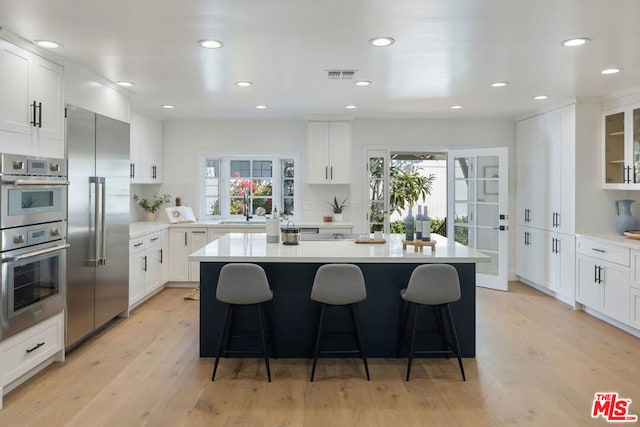 kitchen with a breakfast bar area, stainless steel appliances, light hardwood / wood-style floors, white cabinets, and a kitchen island