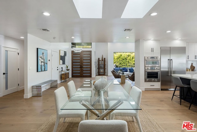 dining space with a skylight and light hardwood / wood-style flooring