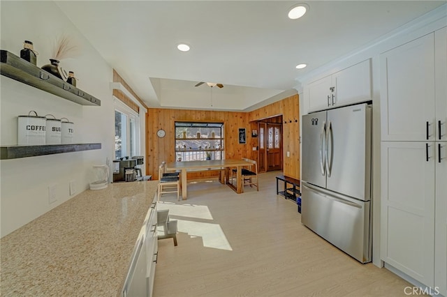 kitchen with light stone counters, light hardwood / wood-style flooring, wooden walls, stainless steel fridge, and white cabinets