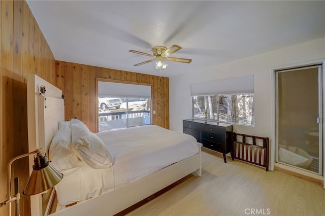 bedroom with ceiling fan, wooden walls, and light wood-type flooring