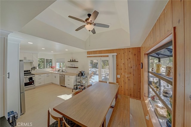 dining area with a raised ceiling, sink, light hardwood / wood-style floors, and wood walls