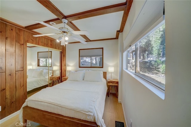 bedroom with beamed ceiling, wood walls, ceiling fan, and light hardwood / wood-style flooring