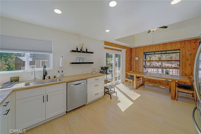 kitchen with wooden walls, white cabinetry, sink, stainless steel dishwasher, and light hardwood / wood-style floors