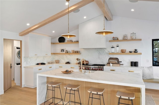 kitchen featuring light stone counters, a kitchen island with sink, a breakfast bar area, and white cabinets