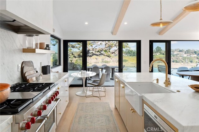 kitchen featuring premium range hood, dishwasher, sink, high end range, and hanging light fixtures