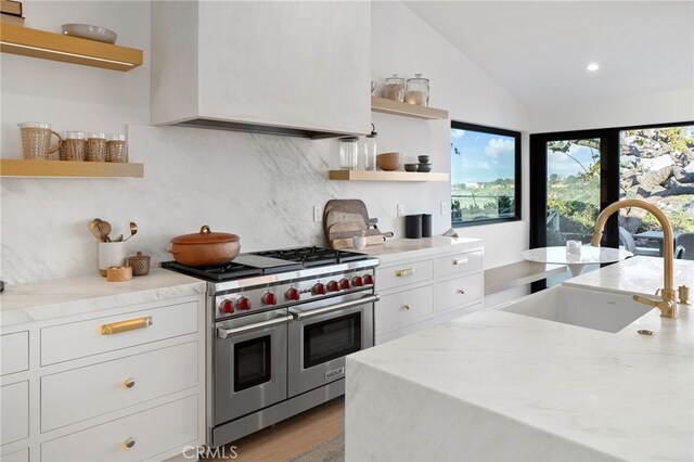 kitchen featuring white cabinetry, sink, range with two ovens, light stone countertops, and custom range hood