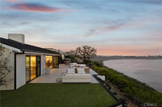 yard at dusk featuring a water view, an outdoor hangout area, and a patio area