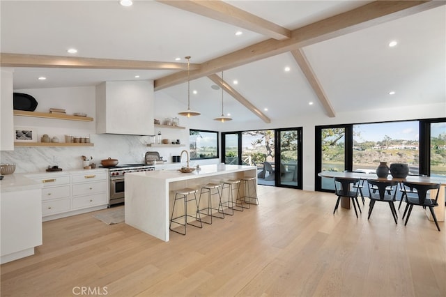 kitchen with pendant lighting, stainless steel stove, a kitchen island with sink, a kitchen breakfast bar, and white cabinets