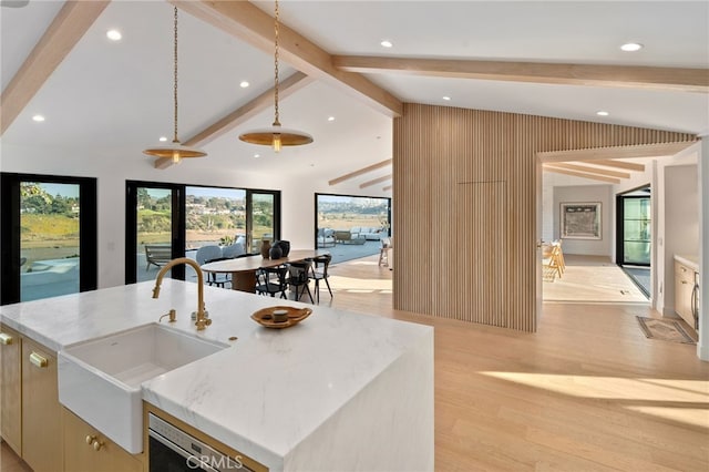 kitchen featuring sink, light hardwood / wood-style flooring, lofted ceiling with beams, and an island with sink