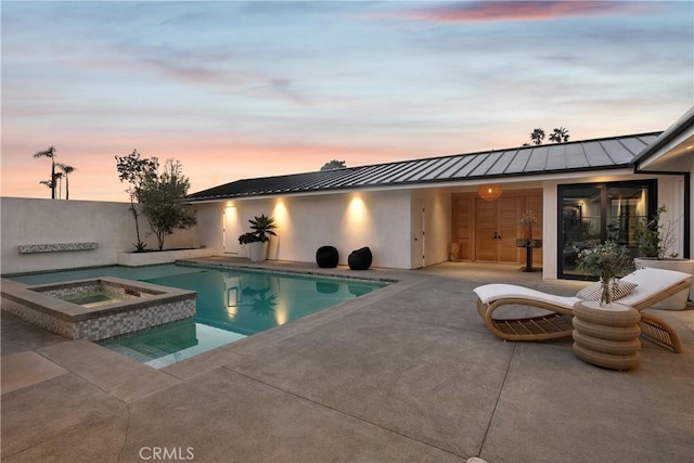 pool at dusk with a patio area and an in ground hot tub