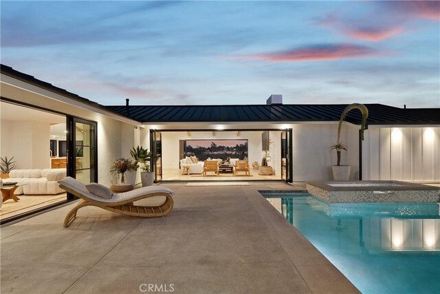 pool at dusk with an outdoor living space, a hot tub, and a patio