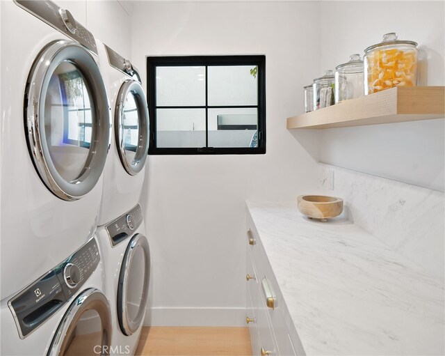 laundry area featuring cabinets, stacked washer / drying machine, and light hardwood / wood-style flooring