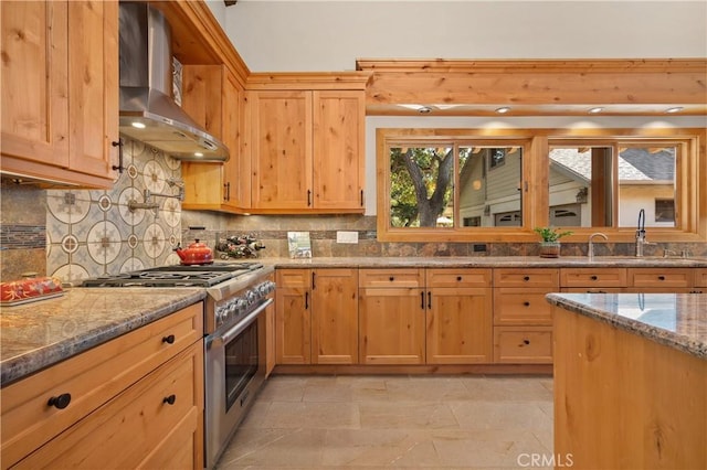 kitchen with sink, tasteful backsplash, high end range, light stone countertops, and wall chimney range hood