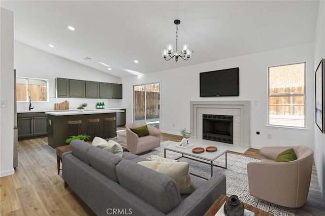 living room featuring sink, a chandelier, vaulted ceiling, light wood-type flooring, and a fireplace