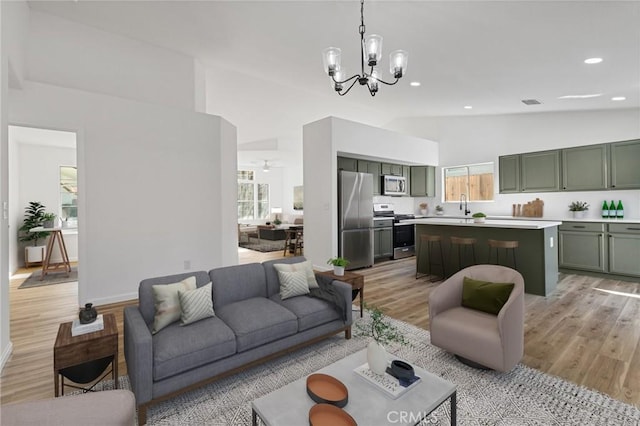 living room with high vaulted ceiling, sink, light hardwood / wood-style flooring, and a notable chandelier