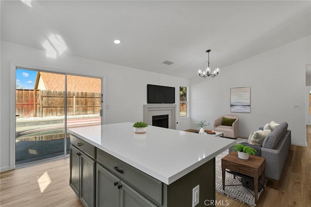 kitchen featuring lofted ceiling, a kitchen island, a notable chandelier, pendant lighting, and light hardwood / wood-style floors