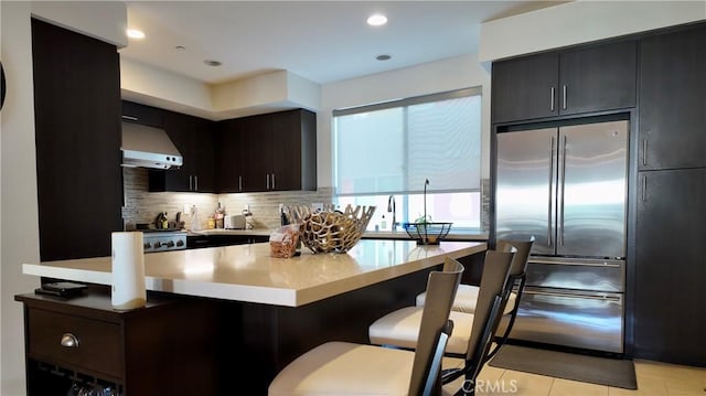 kitchen featuring tasteful backsplash, ventilation hood, a kitchen bar, light tile patterned floors, and stainless steel appliances