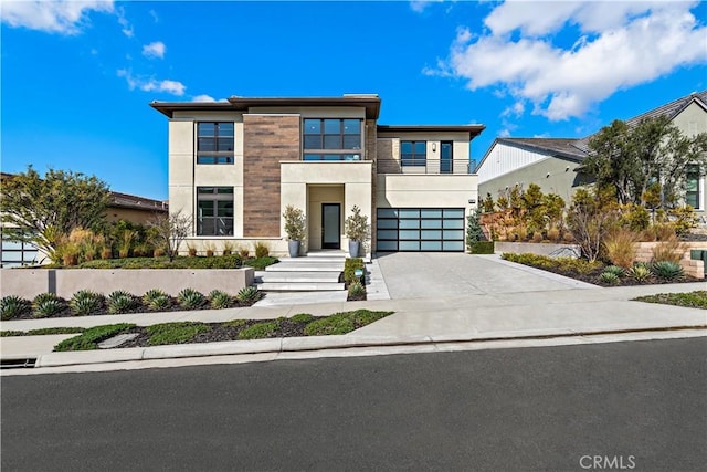 modern home with driveway, an attached garage, a balcony, and stucco siding