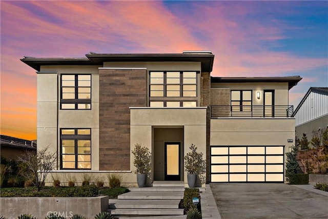 contemporary home featuring driveway, an attached garage, a balcony, and stucco siding