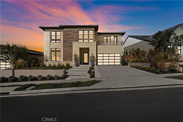 contemporary home featuring a garage, driveway, a balcony, and stucco siding