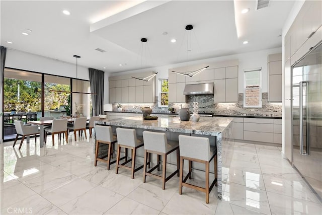 kitchen with a large island, tasteful backsplash, gray cabinets, modern cabinets, and under cabinet range hood