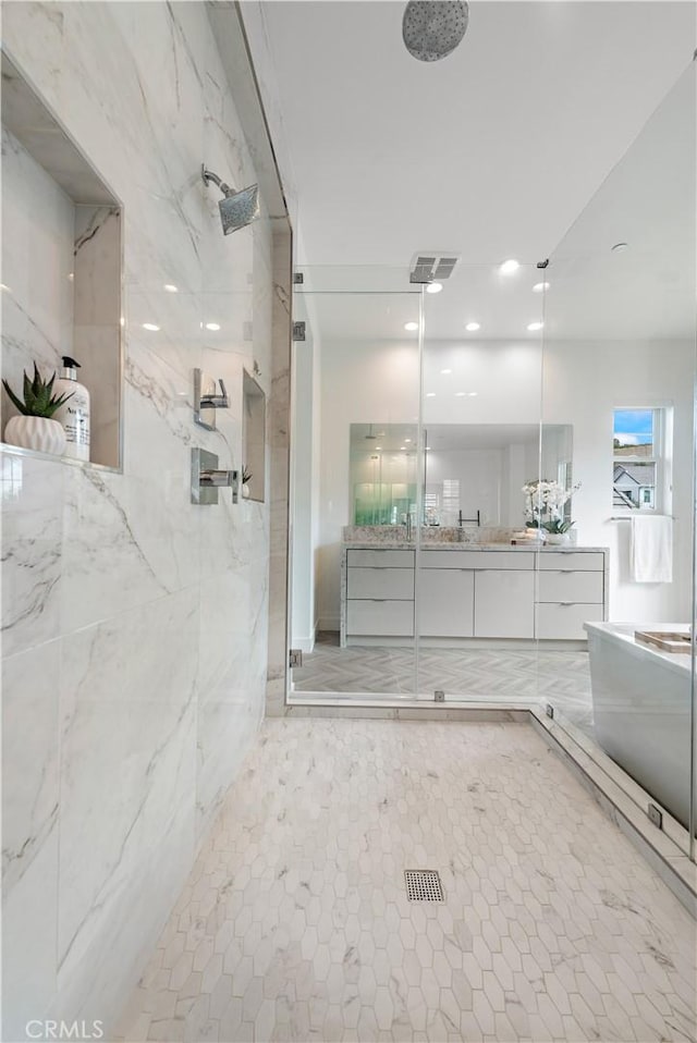 bathroom featuring a bathtub, a marble finish shower, visible vents, and vanity