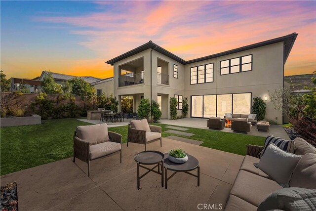 back house at dusk featuring a yard, a patio area, outdoor lounge area, and a balcony