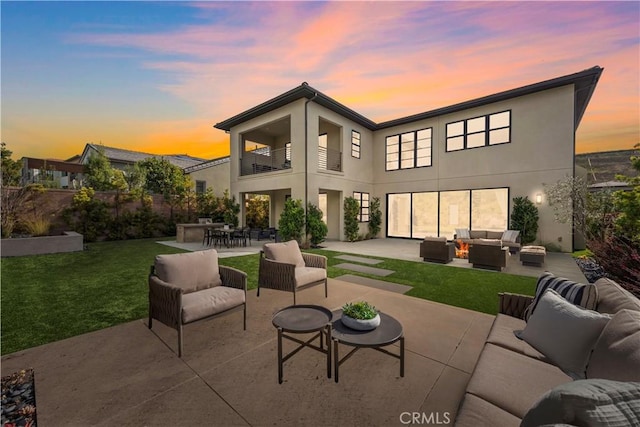 back of property at dusk featuring a lawn, outdoor lounge area, a balcony, and stucco siding