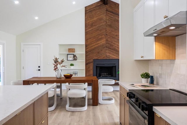 kitchen featuring black range with electric cooktop, light hardwood / wood-style flooring, a large fireplace, and white cabinets