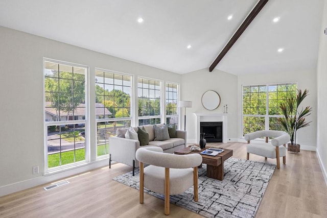 living room featuring plenty of natural light, light hardwood / wood-style floors, and vaulted ceiling with beams