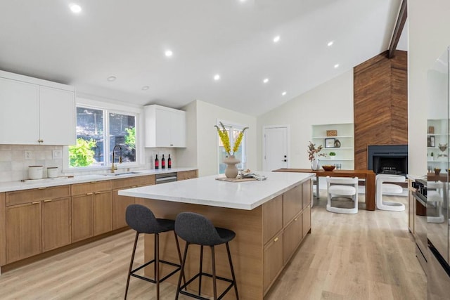 kitchen with sink, a tile fireplace, white cabinetry, light hardwood / wood-style floors, and a kitchen island