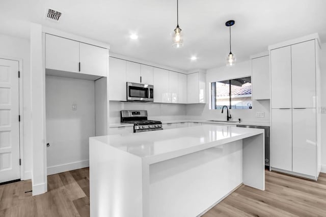 kitchen featuring a kitchen island, appliances with stainless steel finishes, decorative light fixtures, white cabinets, and light hardwood / wood-style flooring