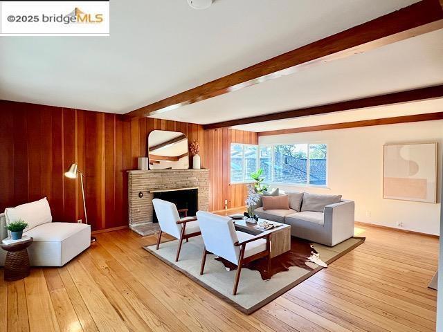 living room featuring wood walls, beam ceiling, a brick fireplace, and light hardwood / wood-style flooring