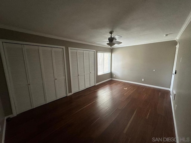 unfurnished bedroom featuring two closets, dark wood-type flooring, ornamental molding, and ceiling fan