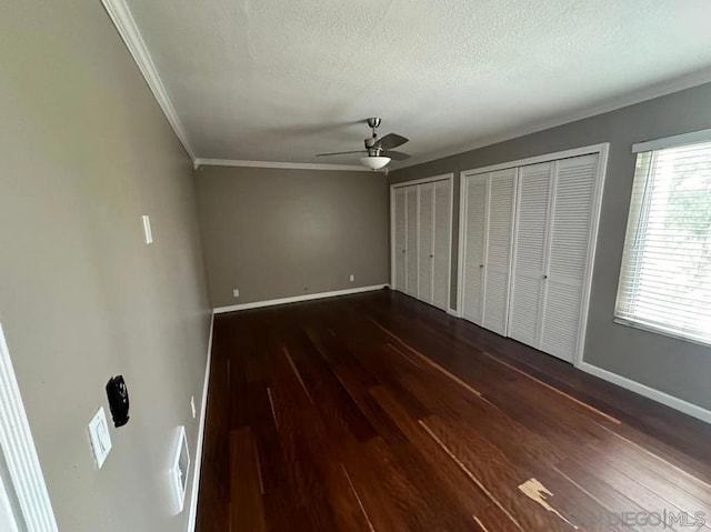 unfurnished bedroom featuring a textured ceiling, ornamental molding, dark hardwood / wood-style flooring, two closets, and ceiling fan