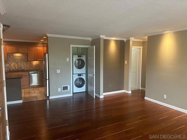 unfurnished living room featuring sink, stacked washing maching and dryer, ornamental molding, a textured ceiling, and dark hardwood / wood-style flooring