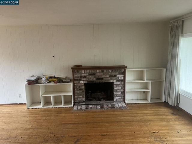 unfurnished living room with wood-type flooring and a brick fireplace