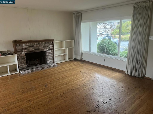 unfurnished living room featuring hardwood / wood-style floors, a brick fireplace, and a wealth of natural light