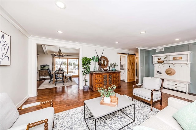 living room featuring ornamental molding, a barn door, wood-type flooring, and a notable chandelier