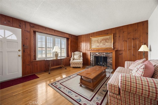 living room with wood walls, a textured ceiling, a fireplace, and light hardwood / wood-style flooring