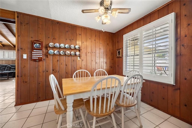 dining area with light tile patterned floors, ceiling fan, and wood walls