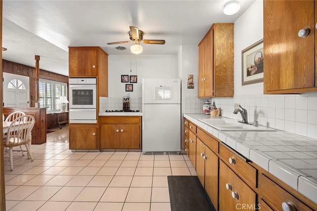 kitchen featuring sink, tile countertops, light tile patterned floors, white appliances, and decorative backsplash