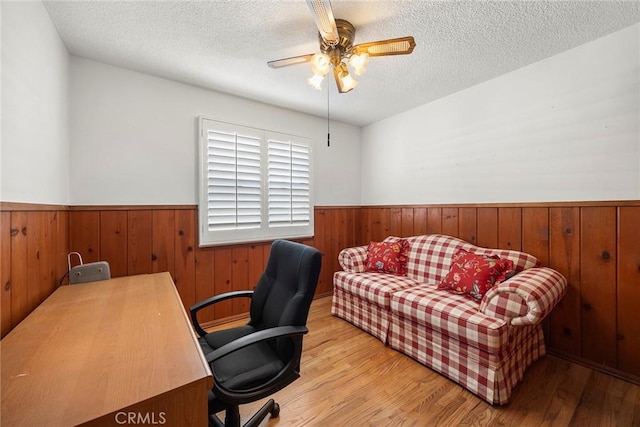 office space featuring ceiling fan, wood walls, a textured ceiling, and light hardwood / wood-style flooring