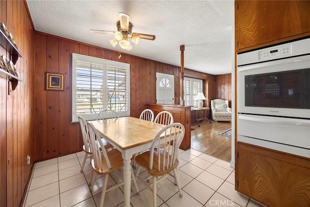 tiled dining room with ceiling fan, a textured ceiling, and wood walls