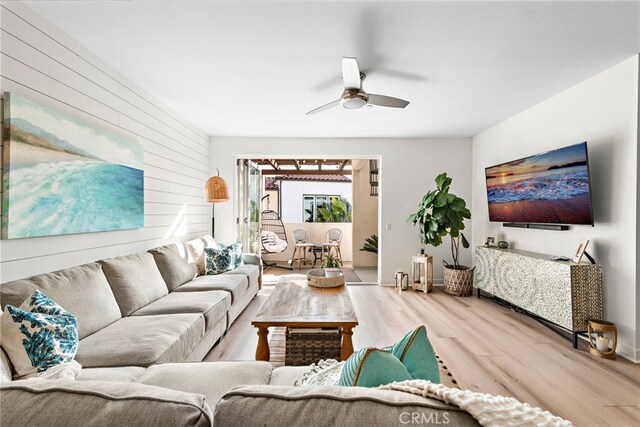 living room featuring ceiling fan, wood-type flooring, and wood walls