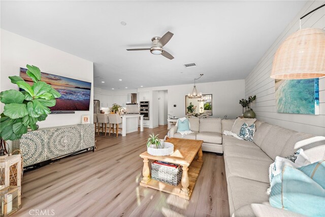 living room with ceiling fan with notable chandelier and light wood-type flooring