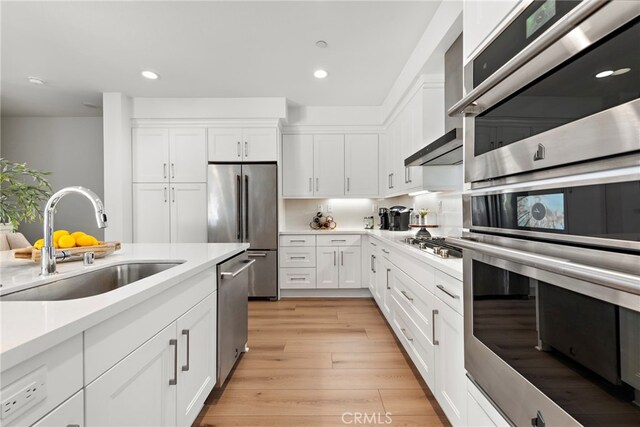 kitchen featuring stainless steel appliances, white cabinetry, sink, and light hardwood / wood-style flooring