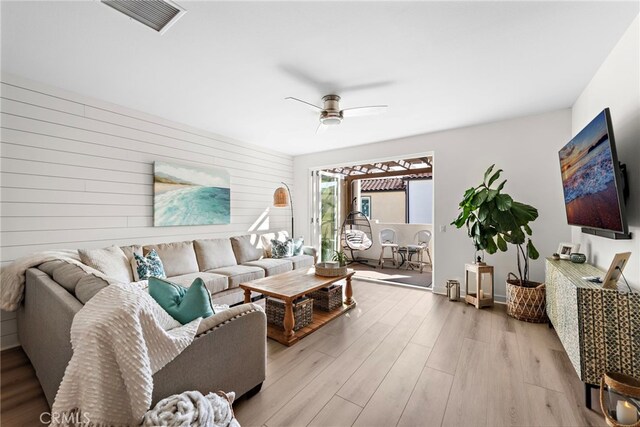 living room featuring light hardwood / wood-style floors, ceiling fan, and wood walls