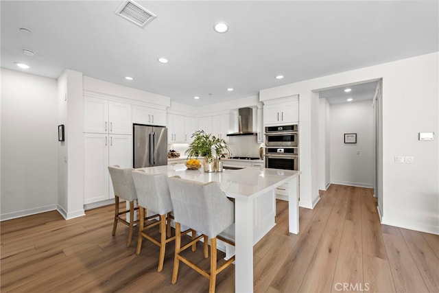 kitchen featuring a breakfast bar, white cabinetry, a kitchen island with sink, stainless steel appliances, and wall chimney exhaust hood