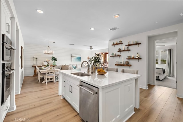 kitchen with white cabinetry, sink, stainless steel appliances, a center island with sink, and light hardwood / wood-style flooring